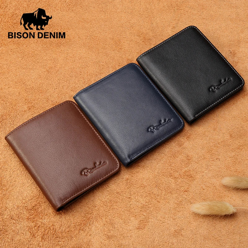 Tres carteras de cuero bifold para hombre, de la marca BISON DENIM, dispuestas diagonalmente sobre un fondo texturizado de color mostaza. Los colores de las carteras son: marrón oscuro, azul marino y negro.