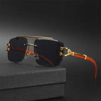 Gafas de sol de estilo lujoso y cuadrado, sin montura, con lentes polarizadas oscuras. Tienen un doble puente superior y detalles metálicos en color dorado. Las patillas presentan un acabado veteado que imita madera marrón claro con un elaborado adorno metálico dorado. Se apoyan sobre una caja negra texturizada.