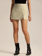 Primer plano de mujer vistiendo una minifalda corta color beige claro con textura suave y una pequeña abertura frontal, combinada con botines negros brillantes.