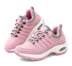 Un par de zapatillas deportivas o de entrenamiento para mujer de color rosa claro. Tienen un diseño robusto con detalles en gris, ojales de metal para los cordones y una suela gruesa blanca.