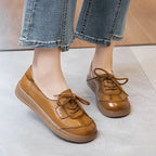 Primer plano de los pies de una persona (probablemente mujer) usando jeans de mezclilla con dobladillos recortados, y un par de zapatos planos y casuales de cuero marrón o caramelo brillante.