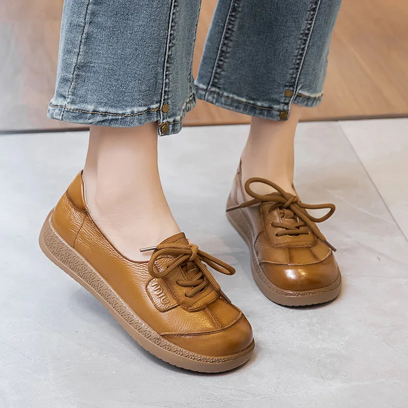 Primer plano de los pies de una persona (probablemente mujer) usando jeans de mezclilla con dobladillos recortados, y un par de zapatos planos y casuales de cuero marrón o caramelo brillante.