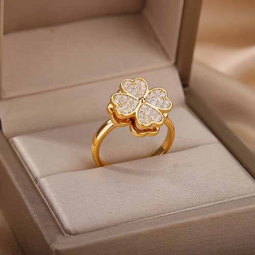 Anillo de compromiso o moda con una flor o trébol que gira, engastado con pedrería pequeña y banda dorada, simbolizando buena suerte.