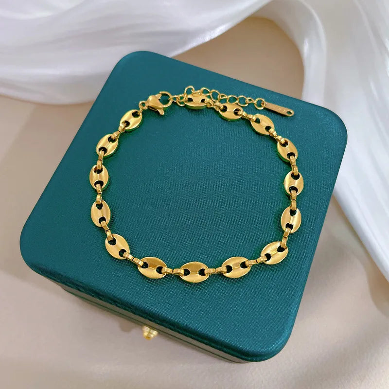 Elegante pulsera de cadena dorada con eslabones tipo grano de café, presentada sobre un estuche de joyería color verde. Accesorio de TicoTrendy.